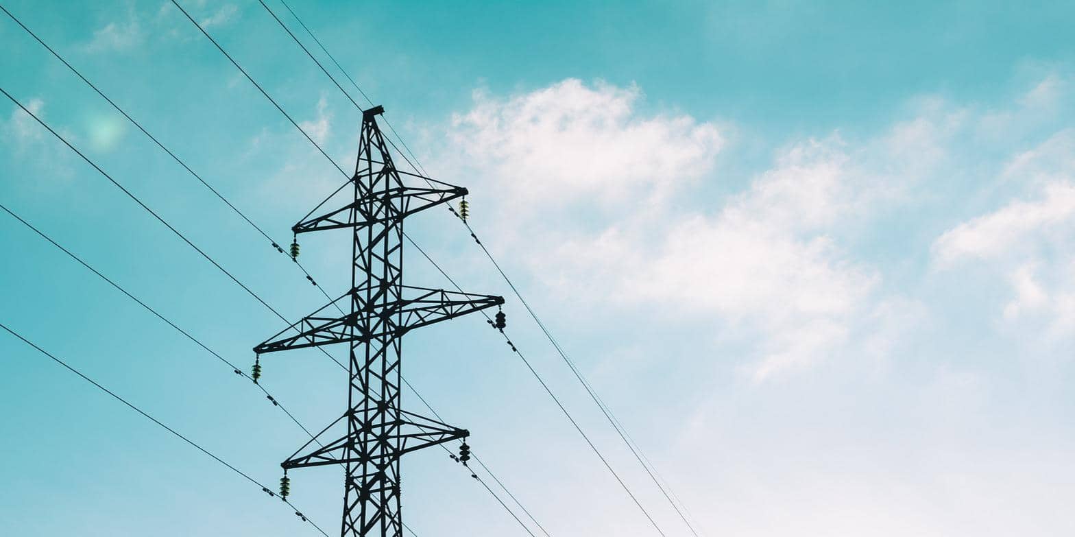 A tall electricity pylon against a clear blue sky with faint clouds, power lines designed to manage electricity extending across the frame.